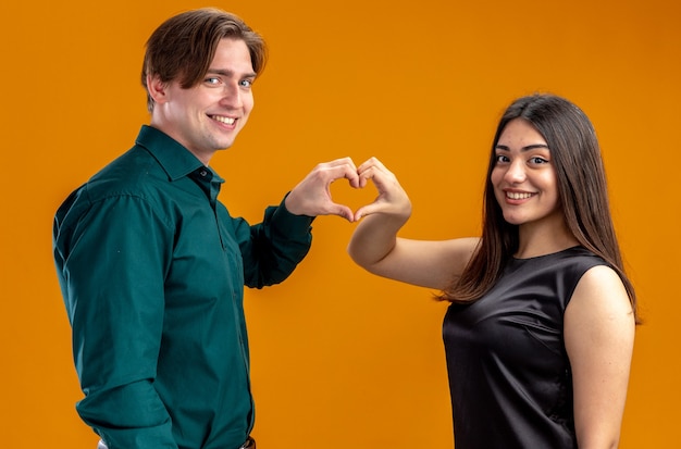 Souriant jeune couple le jour de la Saint-Valentin montrant le geste du coeur isolé sur fond orange