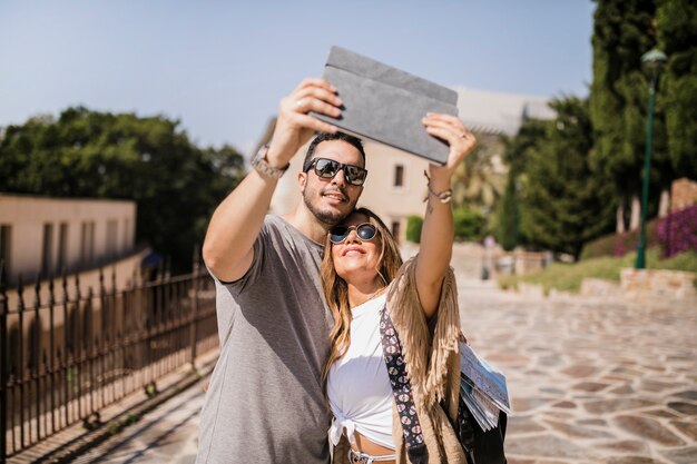 Souriant jeune couple prenant autoportrait sur tablette numérique