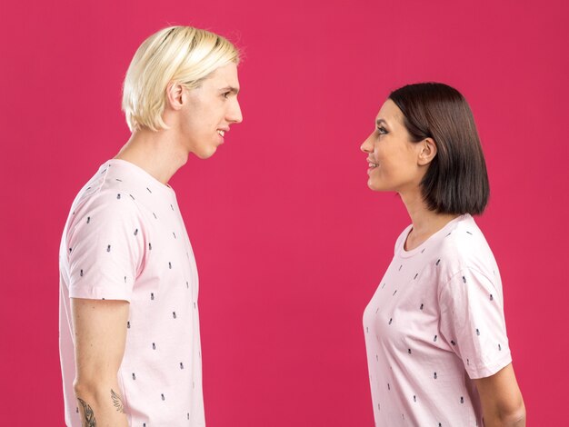 Souriant jeune couple en pyjama debout en vue de profil se regardant isolé sur mur rose