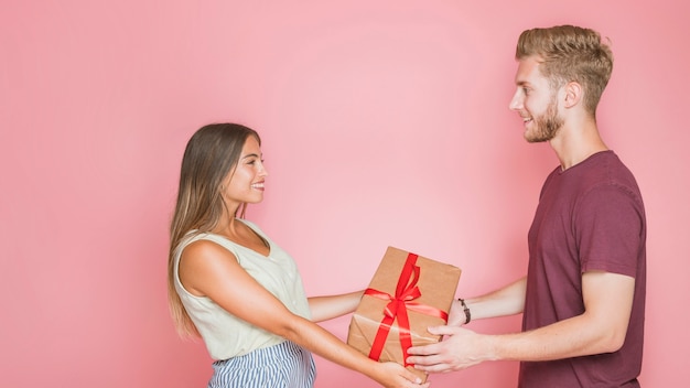 Souriant Jeune Couple Tenant Une Boîte Cadeau Enveloppée Sur Fond Rose