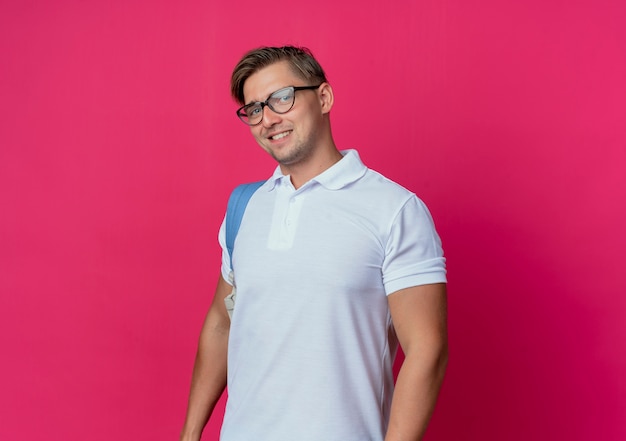 Souriant jeune étudiant beau mâle portant un sac à dos isolé sur rose