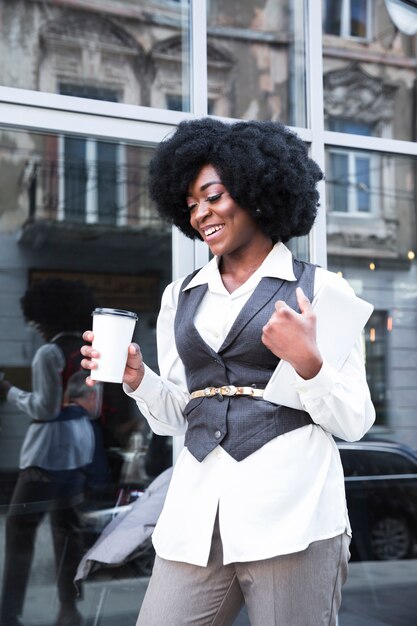 Souriant jeune femme d&#39;affaires africaine tenant la tasse de café à emporter et tablette numérique à la main