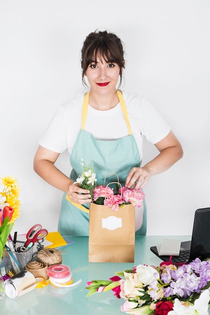 Souriant jeune femme fleuriste avec sac de papier fleur sur le bureau