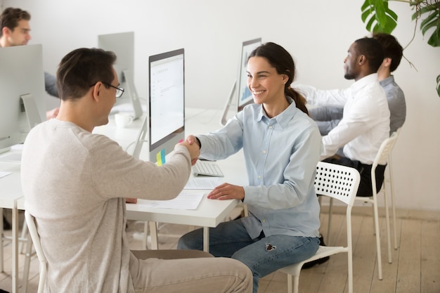 Souriant jeune femme handshaking client satisfait faisant affaire au bureau