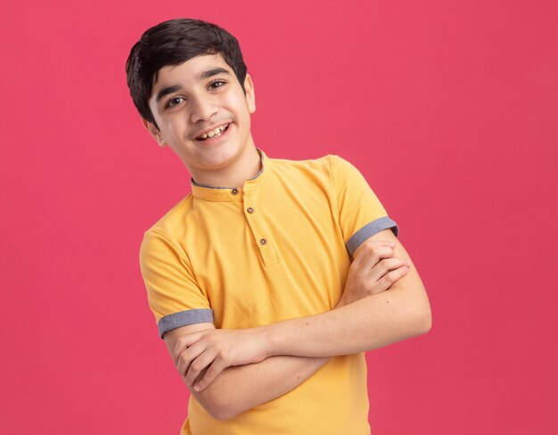 Souriant jeune garçon caucasien debout avec une posture fermée isolée sur un mur rose