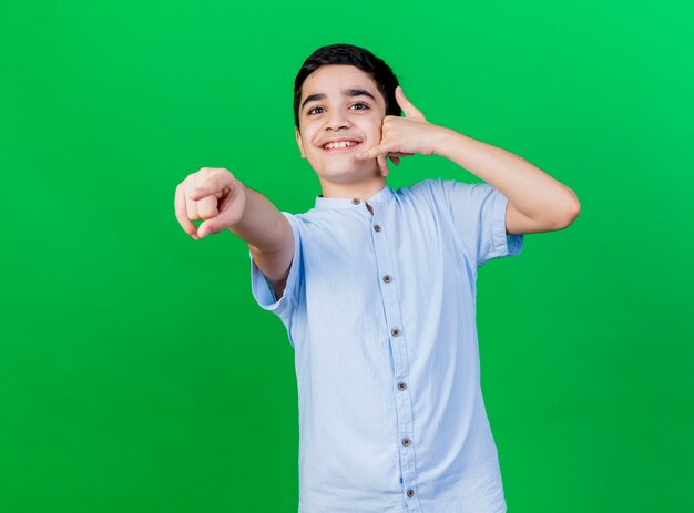 Souriant jeune garçon caucasien regardant et pointant vers la caméra faisant le geste d'appel isolé sur fond vert avec espace copie