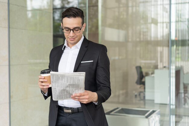 Souriant jeune homme d&#39;affaires avec café lecture journal à l&#39;extérieur