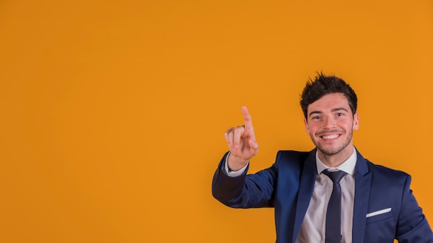 Photo gratuite souriant jeune homme d'affaires contre pointant son doigt vers le haut sur fond orange