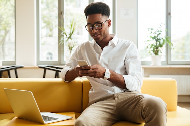 Souriant jeune homme africain assis coworking discuter par téléphone.