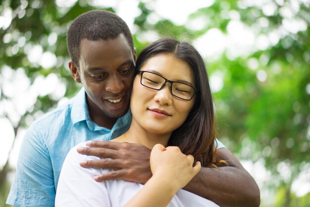 Souriant jeune homme afro-américain embrassant une femme asiatique heureuse.