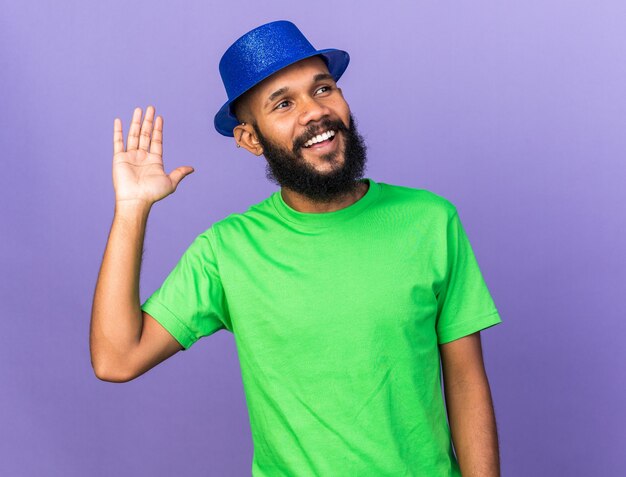 Souriant jeune homme afro-américain portant un chapeau de fête montrant un geste de bonjour