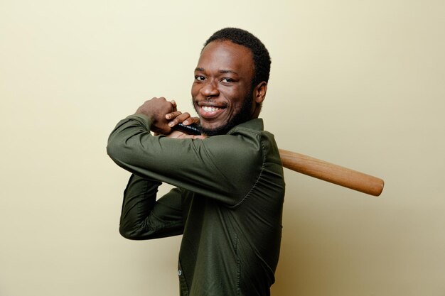 Souriant jeune homme afro-américain portant une chemise verte tenant une batte de baseball isolée sur fond blanc