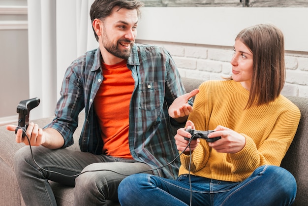 Souriant jeune homme assis sur un canapé jouant avec une manette de jeu