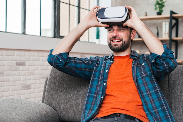 Photo gratuite souriant jeune homme assis sur un canapé portant une caméra de réalité virtuelle