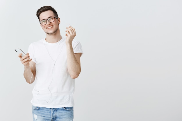 Souriant jeune homme au décollage écouteurs, tenant le smartphone