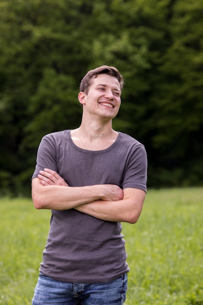 Photo gratuite souriant jeune homme aux bras croisés dans la nature