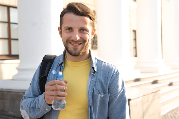 Photo gratuite souriant jeune homme barbu tenant une bouteille d'eau et regardant la caméra