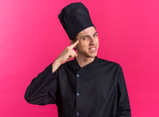 Souriant jeune homme blond cuisinier en uniforme de chef et casquette faisant un geste de réflexion