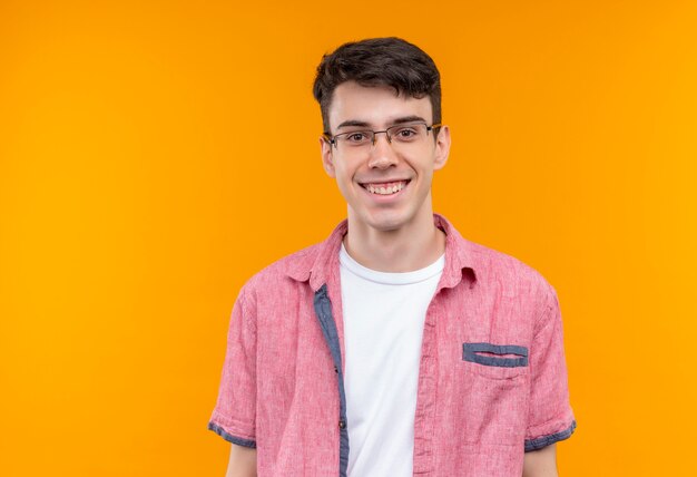 Souriant jeune homme caucasien portant chemise rose dans des verres sur fond orange isolé