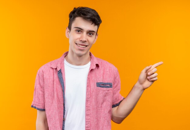 Souriant jeune homme caucasien portant chemise rose pointe à côté sur fond orange isolé