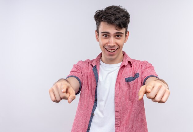 Souriant jeune homme caucasien portant chemise rose vous montrant le geste avec les deux mains sur fond blanc isolé