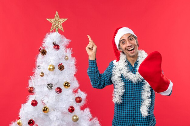 Souriant jeune homme avec chapeau de père Noël dans une chemise rayée bleue et portant sa chaussette de Noël