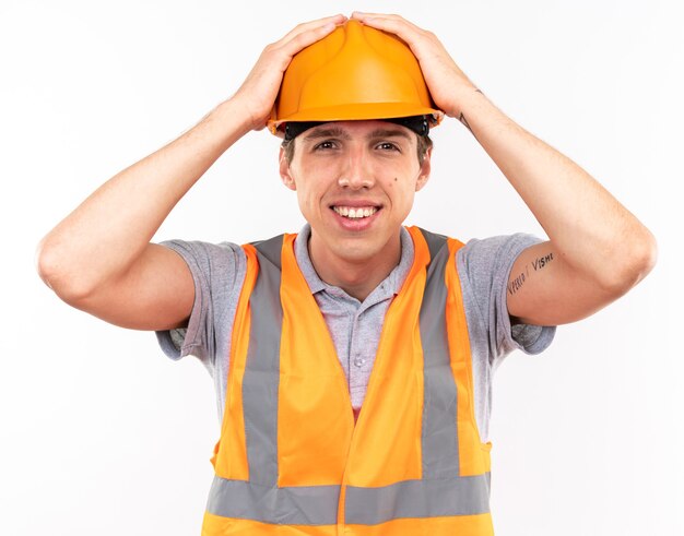 Souriant jeune homme constructeur en uniforme a attrapé la tête isolée sur un mur blanc