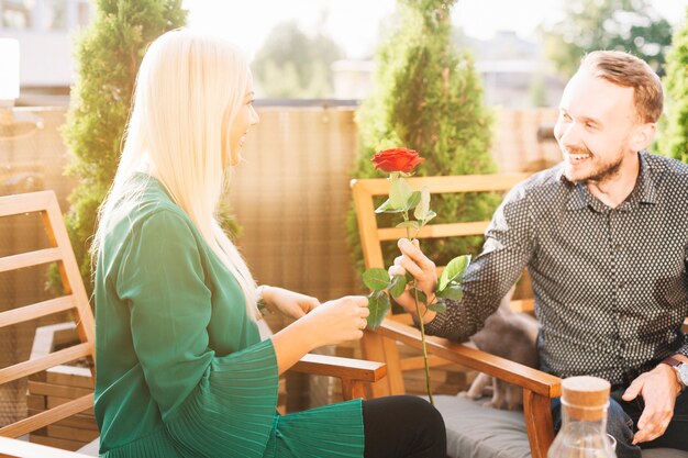 Souriant jeune homme donnant rose rouge à sa copine blonde