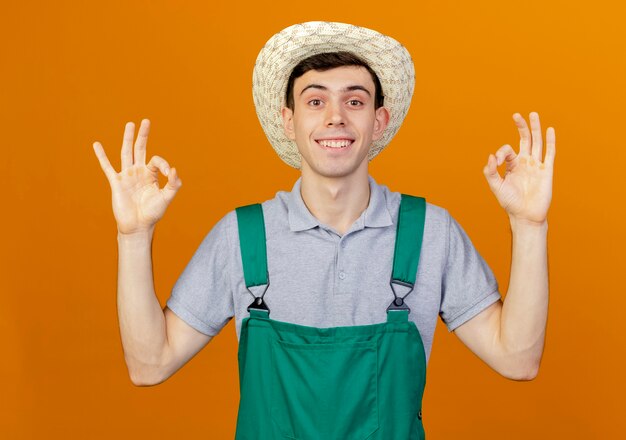 Souriant jeune homme jardinier portant des gestes de chapeau de jardinage signe de la main ok avec les deux mains