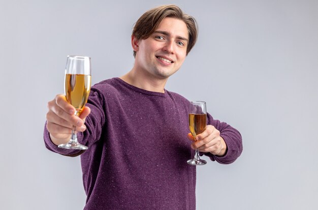 Souriant jeune homme le jour de la Saint-Valentin tenant des verres de champagne à la caméra isolé sur fond blanc