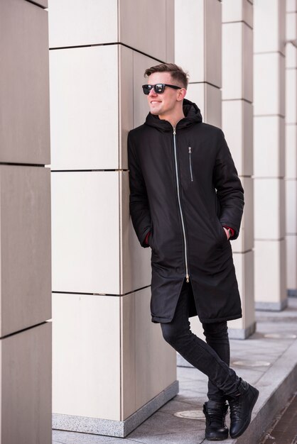 Souriant jeune homme avec les mains dans la poche se penchant sur le mur