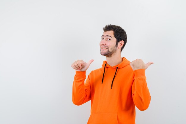 Souriant jeune homme montrant la droite avec ses pouces sur fond blanc