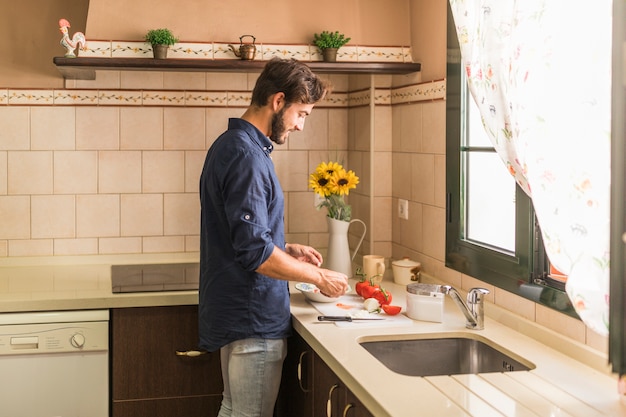 Souriant jeune homme préparant une salade dans la cuisine