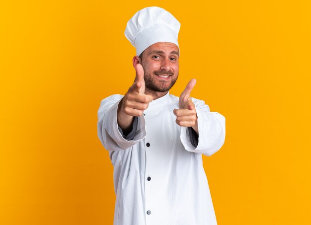 Souriant jeune homme de race blanche cuisinier en uniforme de chef et casquette faisant le geste du pistolet