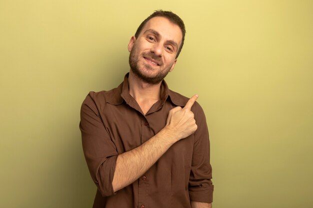 Souriant jeune homme regardant avant pointant sur le côté isolé sur mur vert olive