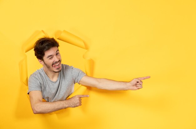 Souriant jeune homme regardant du visage de gars de vente de fond de papier jaune déchiré