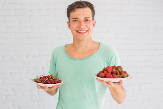 Photo gratuite souriant jeune homme tenant des assiettes de fraises et de cerises