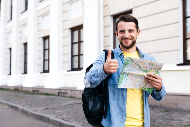 Souriant jeune homme tenant la carte et montrant le pouce vers le haut de geste à l'extérieur