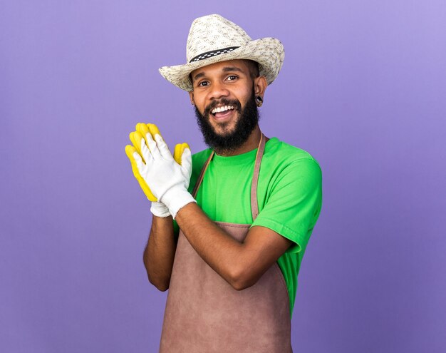 Souriant jeune jardinier afro-américain portant un chapeau de jardinage avec des gants se tenant la main