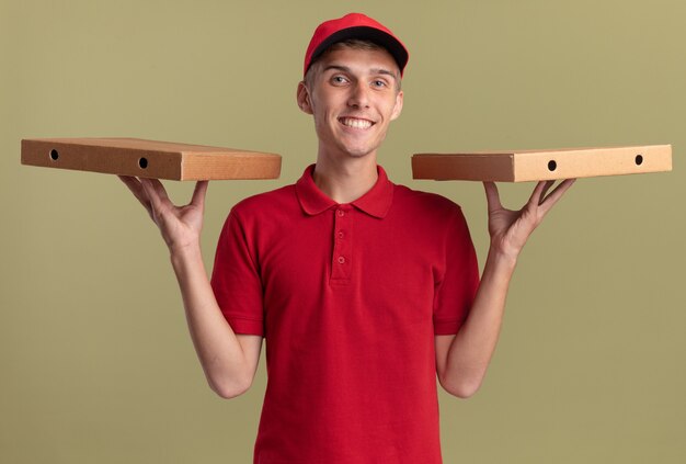 Souriant jeune livreur blond tient des boîtes à pizza sur les mains