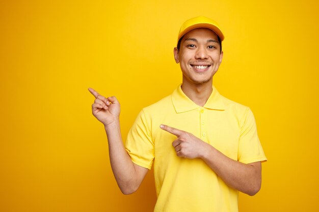 Souriant jeune livreur portant casquette et uniforme pointant vers le haut au coin