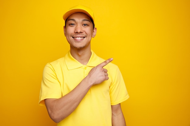 Souriant jeune livreur portant casquette et uniforme pointant vers le haut au coin