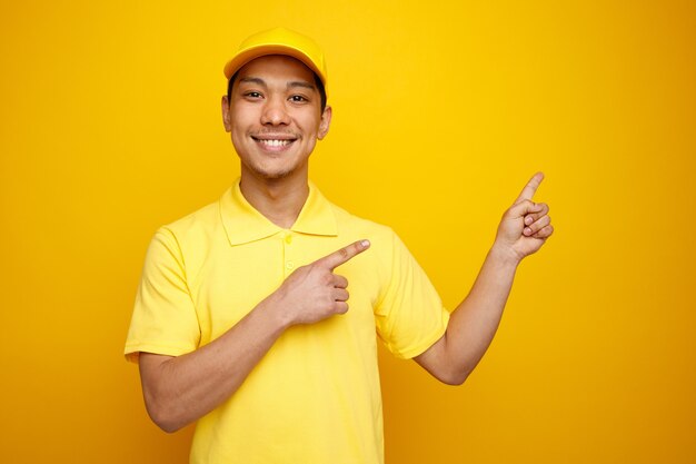 Souriant jeune livreur portant casquette et uniforme pointant vers le haut au coin