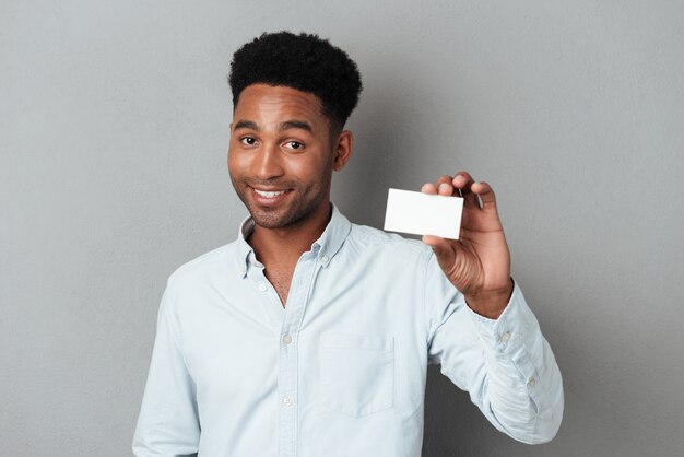 Souriant jeune mec afro américain tenant une carte de visite vierge