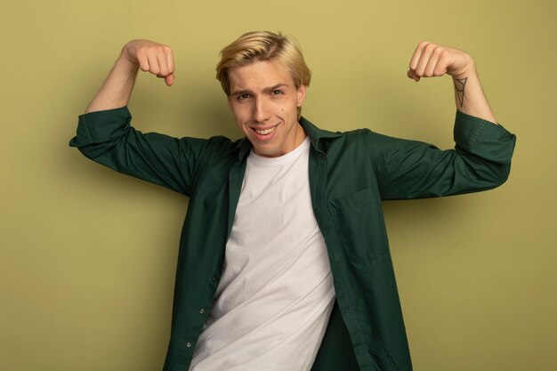 Souriant jeune mec blond portant un t-shirt vert montrant un geste fort