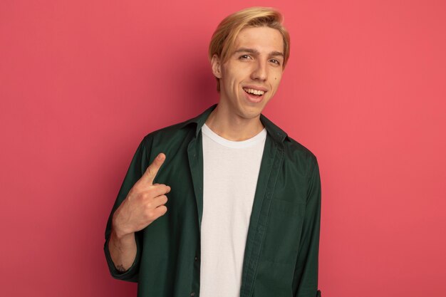 Souriant jeune mec blond vêtu d'un point de t-shirt vert vers le haut