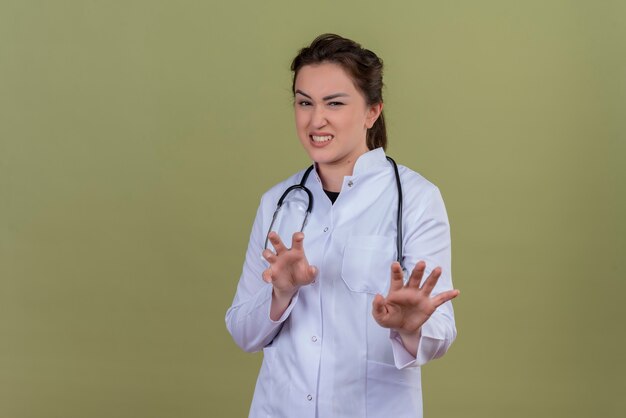 Souriant jeune médecin portant une blouse médicale portant un stéthoscope montre le geste du tigre sur le mur vert