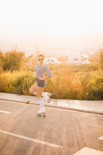 Souriant jeune patineuse debout sur une jambe posant sur la route