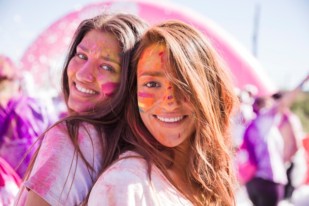 Souriant jeunes femmes avec la couleur holi sur leur visage debout dos à dos