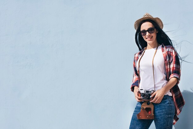 Souriant jolie femme tenant la caméra debout contre le mur bleu